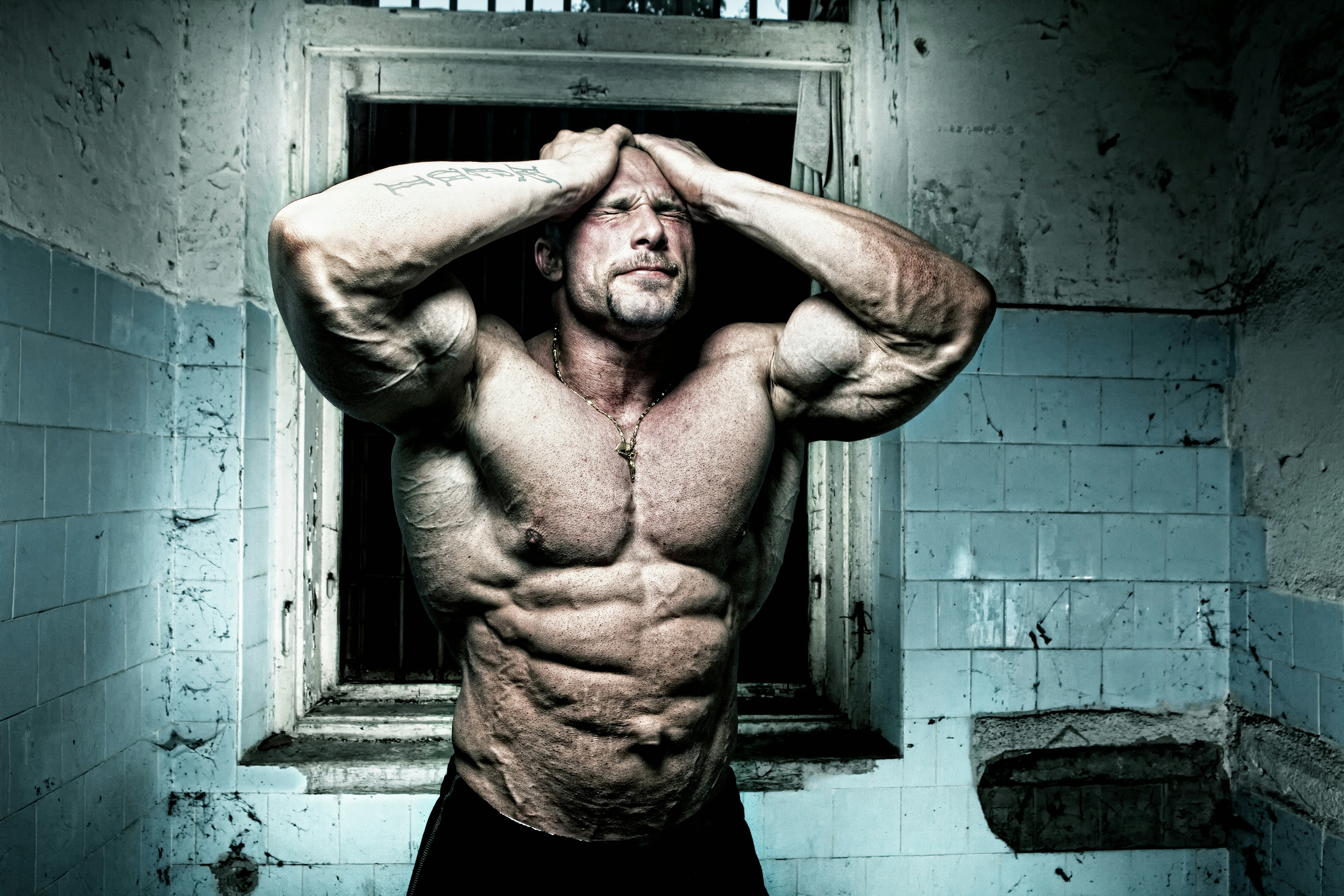 man in black tank top leaning on blue brick wall